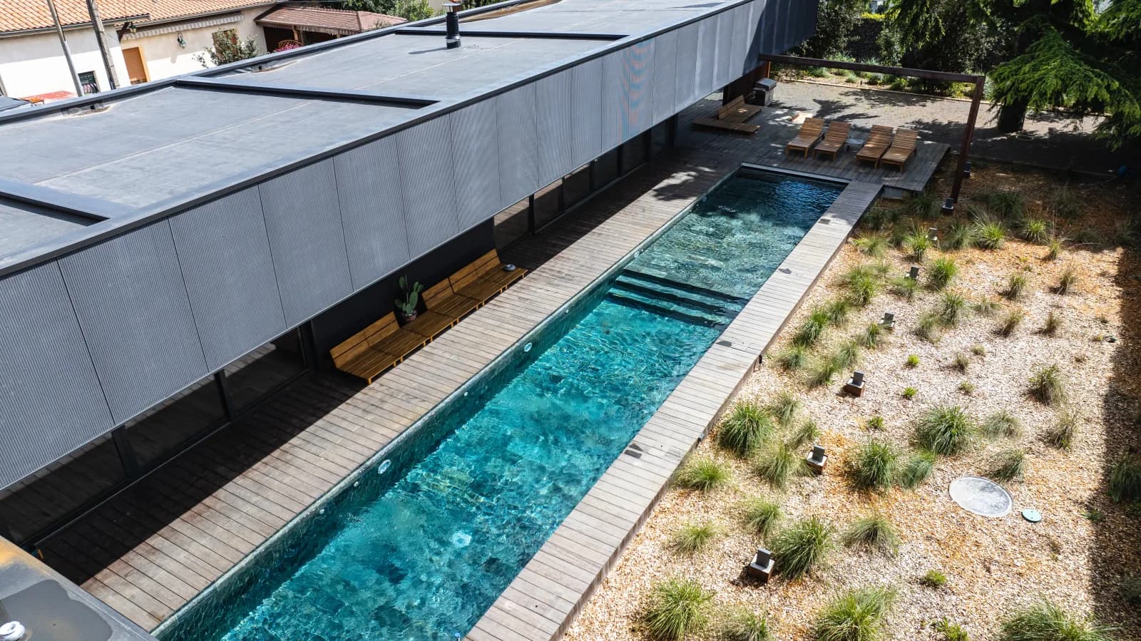 Pool and wooden deck along a building, seen from the drone
