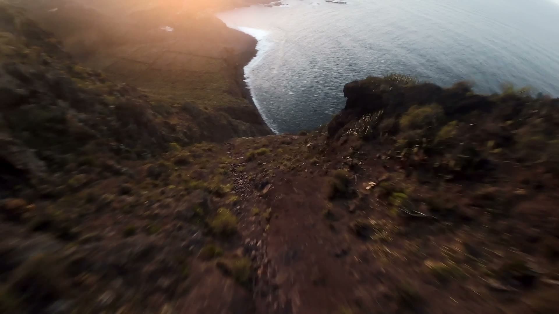 FPV drone diving along a cliff towards the sea at sunset