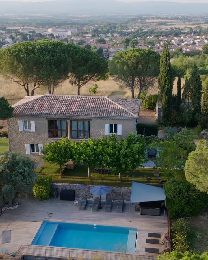 Aerial view of a stone house with a pool, surrounded by pine trees