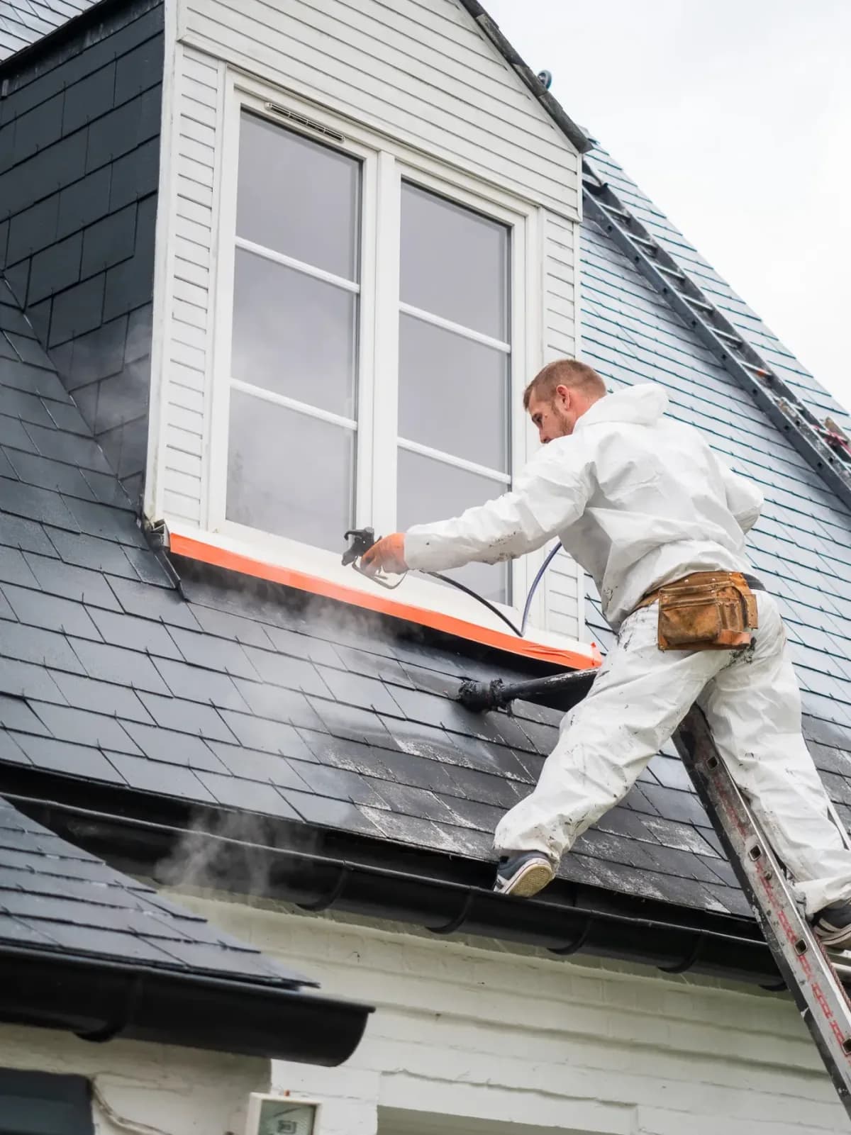 Tradesman on a ladder by the dormer window of a slate roof