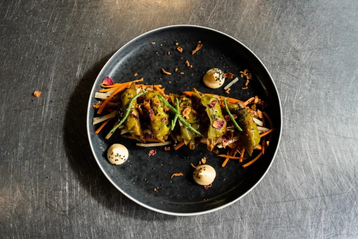 Thin ribbons of vegetables on a black plate, set on a stainless steel counter
