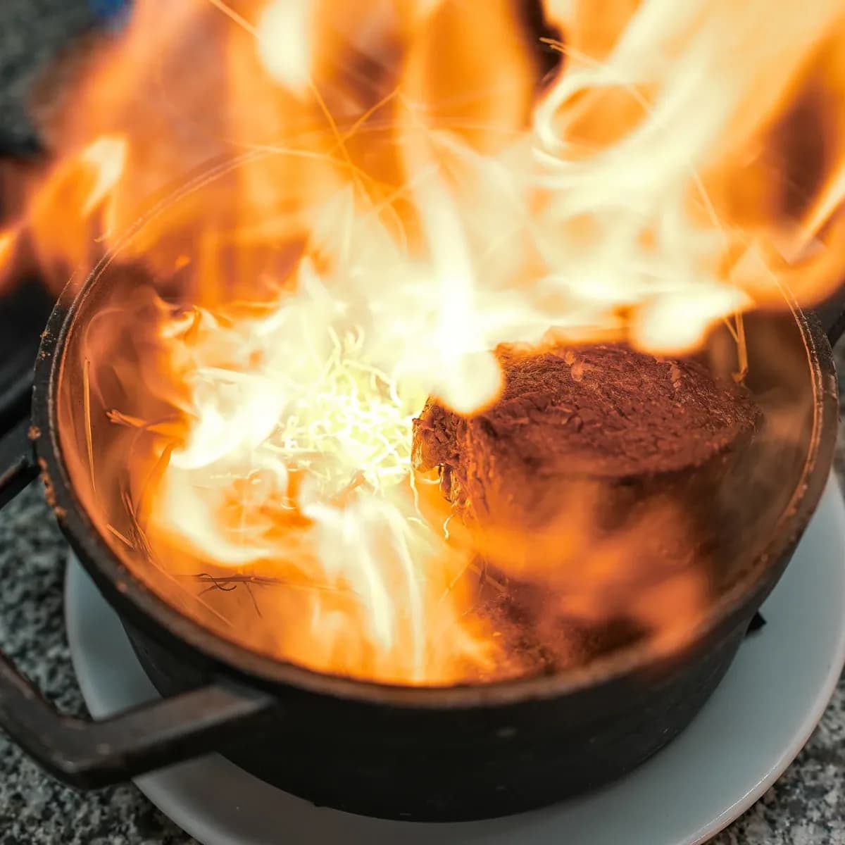 Cast-iron pot being flambéed in a kitchen