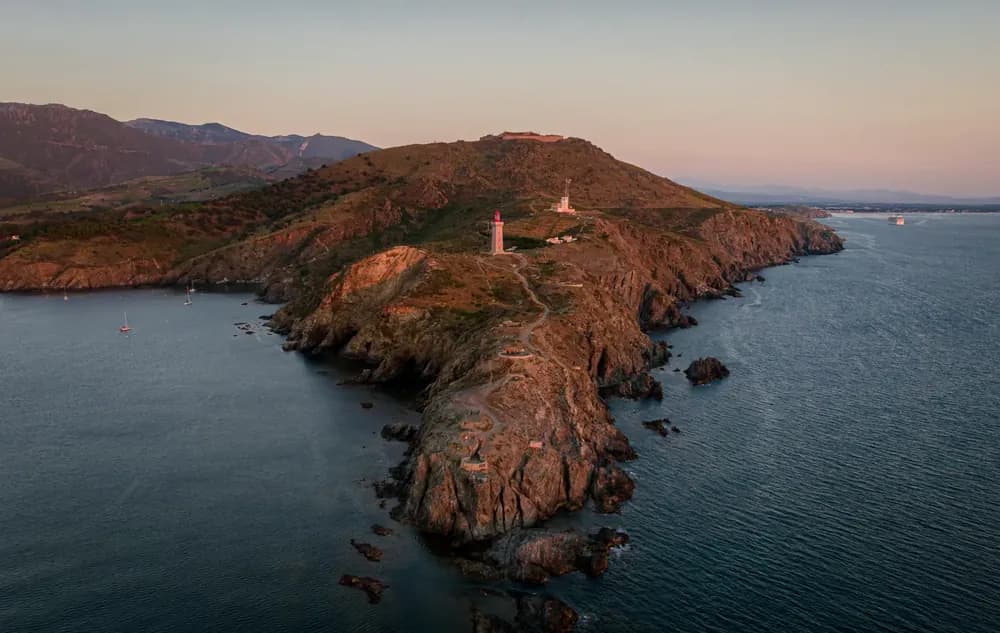 A rocky headland above the sea at sunset, seen from a drone