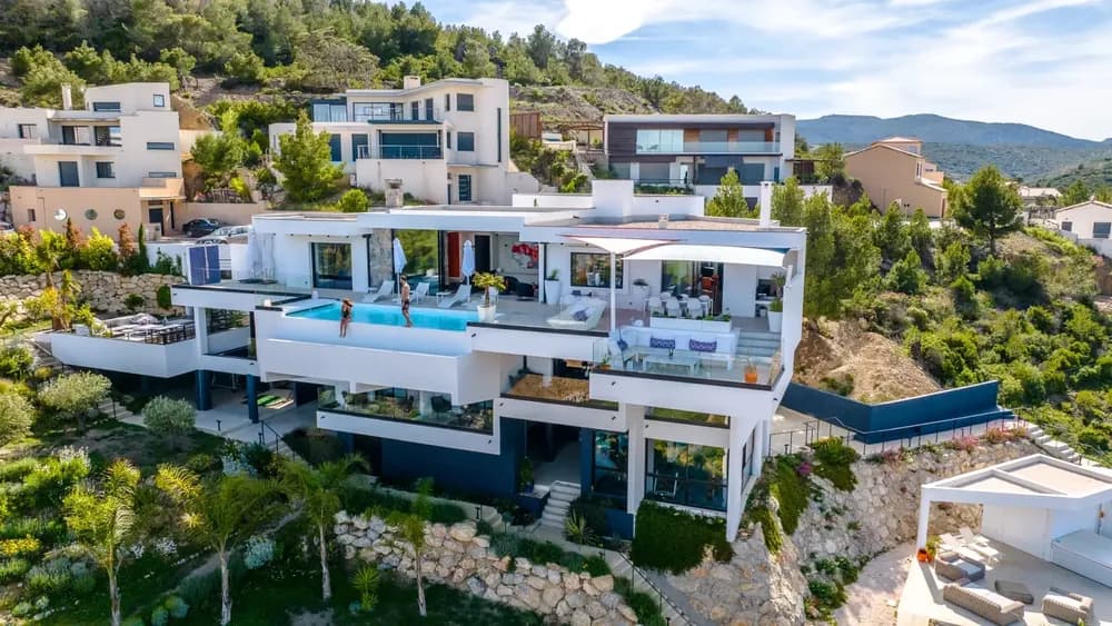 A white villa with a pool on a hillside, seen from a drone