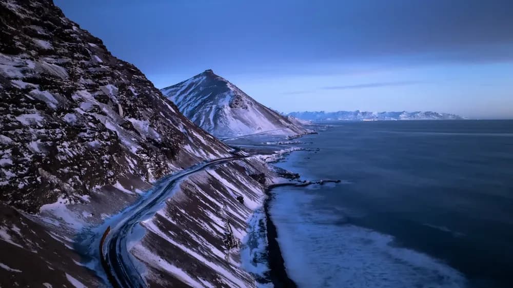 A coastal road beneath a mountain, at dusk