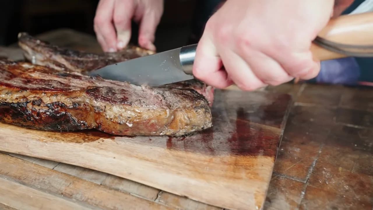 The chef carves a grilled rib of beef, then slices the pink meat